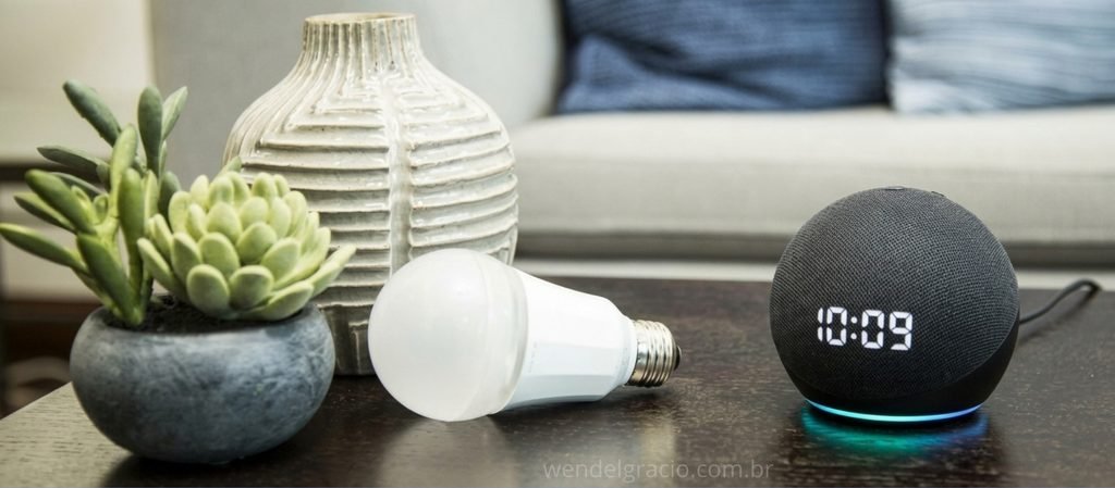 Uma lampada smart e uma echo dot com relógio sobre uma mesa em uma sala